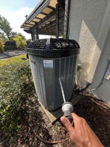 Person rinsing air conditioner coils with an outdoor hose