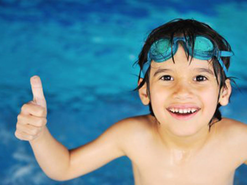 A kid in a pool showing thumbs up