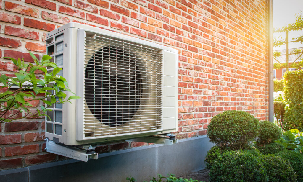 Angled shot of a wall-mounted air source heat pump against a brick wall