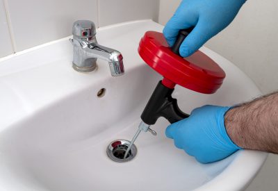 Plumber with blue gloves using drain snake for bathroom sink clog