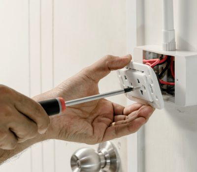 The electrician is using a screwdriver to attach the power cord to the wall outlet