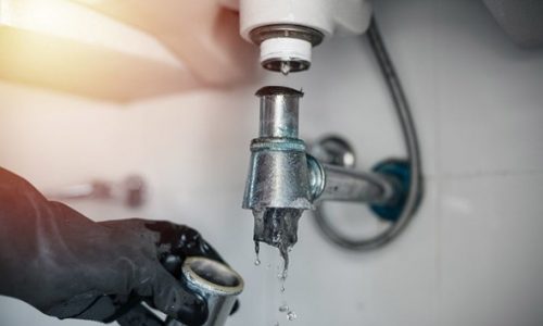 Plumber fixing pipe connection under bathroom sink